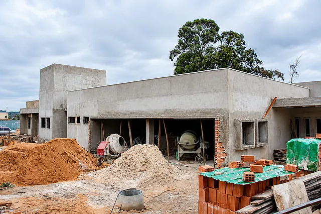 Obra em andamento com duas betoneiras, montes de areia e paredes de uma construção em fase de reboco