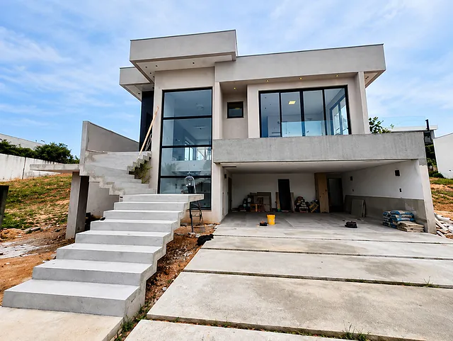 Casa moderna de dois andares com grandes janelas de vidro e escadaria de concreto, em fase final de obra